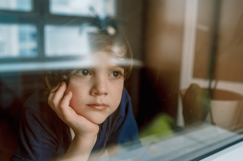 Thoughtful boy looking through glass window